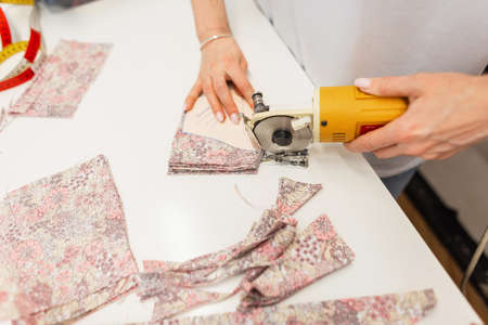 Fashion designer woman with electro-cutter cuts fabric in studio, close-upの写真素材