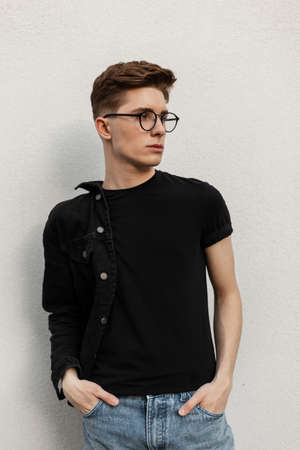 Fresh portrait of confident young man with hairstyle in fashionable black denim clothes in stylish...