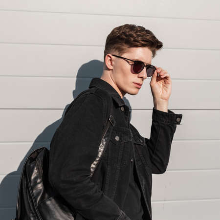 Fresh portrait fashionable young man in stylish denim black jacket in trendy sunglasses with...
