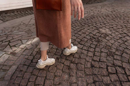 Fashionable woman in elegant long coat in pants in stylish footwear walks in the city. Close-up...