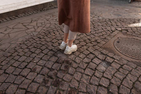 Fashionable young woman in long elegant coat in beige pants in leather stylish youth sneakers....