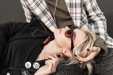 Fresh portrait of pretty young blonde woman in fashionable black blazer in stylish sunglasses. Cute girl fashion model in vintage clothes is resting on friend's legs. Trendy sisters relaxes outdoors.の写真素材