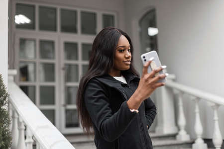 Stylish beautiful african business woman with smartphone making video call in the city. Girl taking a selfieの写真素材