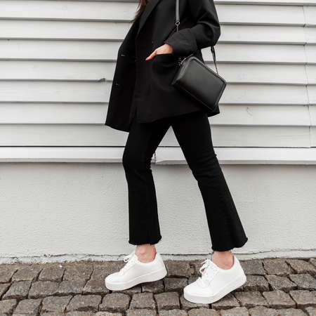 Cool girl in fashion denim pants in leather stylish sneakers in trendy jacket with black handbag...