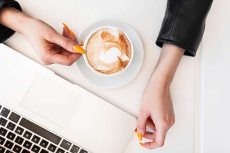 Close-up of a desktop with cup of hot coffee and modern laptop, behind with girl in black stylish...
