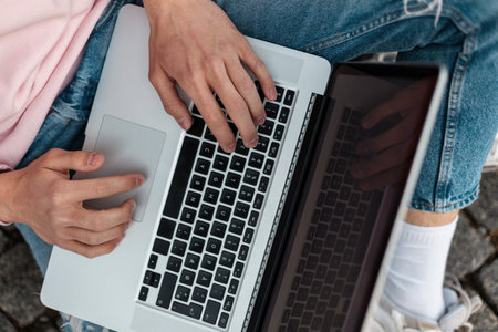 Close-up of male hands with laptop. Business stylish man freelancer sitting on street and typing on...