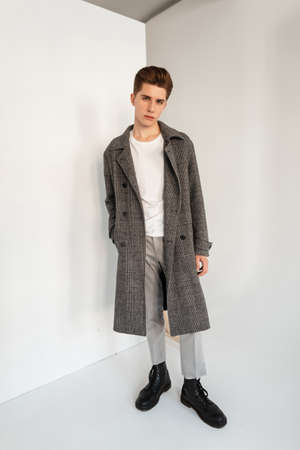Handsome young stylish elegant man in trendy casual clothes with coat in studio