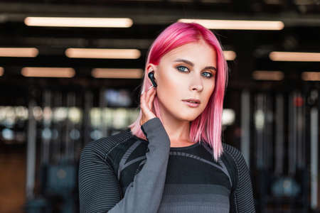 Portrait of sporty beautiful woman model with pink hair with wireless headphones working out in the...