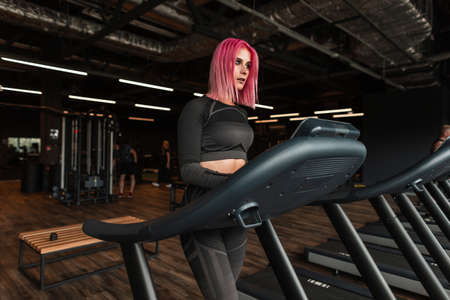 Beautiful young woman with black stylish sportswear running on a treadmill in the gym