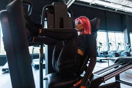 Beautiful sportive woman trains and does exercises for pumping leg muscles in the gym