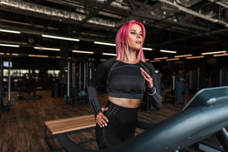 Young fitness woman in black fashionable sportswear running on a treadmill in the gym