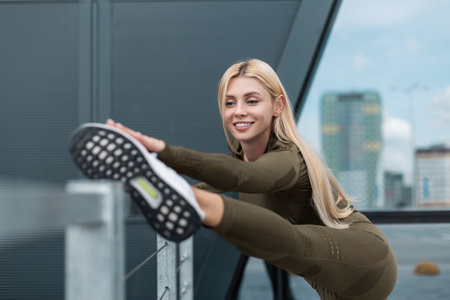 Beautiful happy young fitness woman with cute smile and slender body in fashion green sportswear with running sneakers doing exercise stretching and warm up in the cityの写真素材