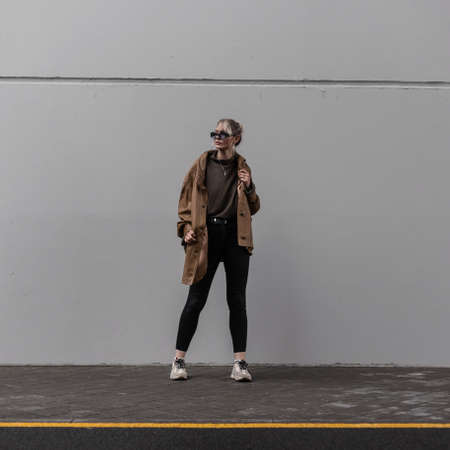 Cool stylish girl in street clothes stands near a gray wall in the cityの写真素材
