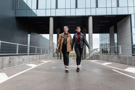 Two pretty teen girls in fashionable leather outfit with a jacket and black jeans are walking in the cityの写真素材