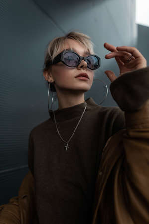 Fashionable portrait of a beautiful young girl model in stylish sunglasses in a brown jacket and sweater in the cityの写真素材