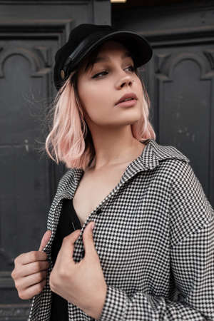 Urban beautiful young stylish woman in fashionable clothes with stylish cap on the background of a...