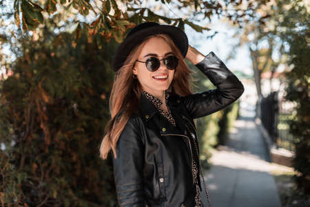 Happy portrait of a beautiful young girl model in fashionable clothes look with a leather jacket and stylish sunglasses walks in the autumn parkの写真素材