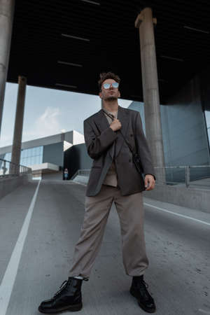 Handsome fashionable business man model in stylish gray suit with boots and sunglasses on urban backgroundの写真素材