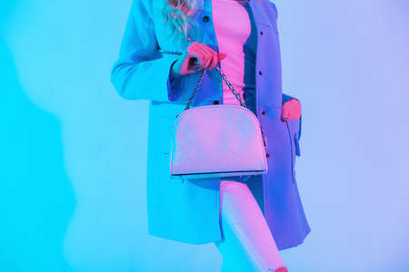 Beautiful stylish woman in colored blue blazer, blouse and jeans with white fashionable handbag in the studio at neon pink light. Close-up of a leather female bagの写真素材