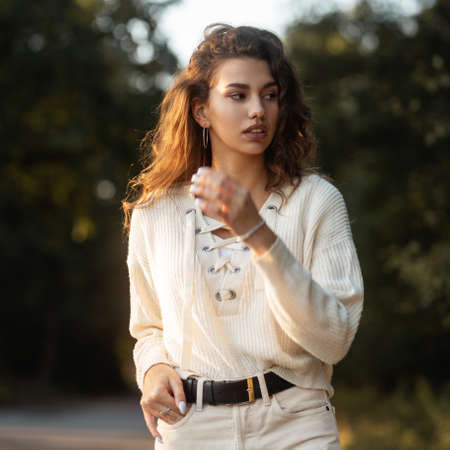 Fresh portrait of a beautiful curly-haired woman model in a knitted fashionable blouse walks...