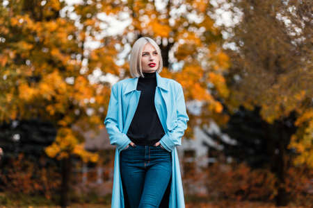 Pretty blonde business woman in fashion blazer, sweater and jeans walks in orange autumn parkの写真素材