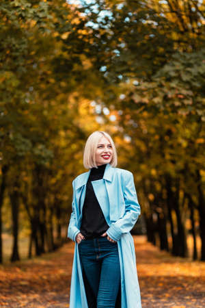 Pretty young happy woman with blue fashion coat walks on autumn parkの写真素材