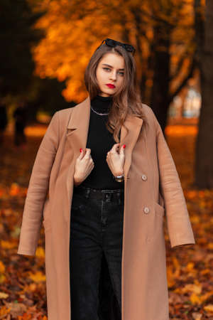 Beautiful young fashionable woman in a stylish beige coat and sweater walks in an autumn park with...