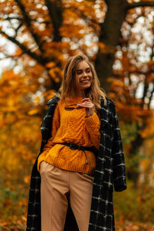 Fashionable beautiful smiling girl in stylish autumn clothes is walking in a golden fall park with yellow foliageの写真素材
