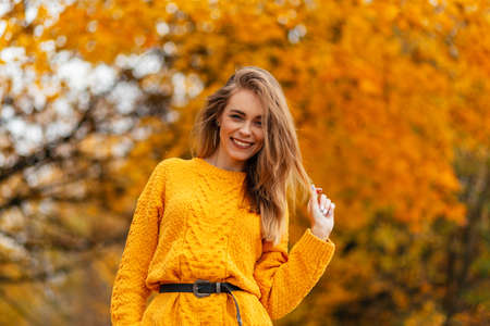 Smiling stylish happy woman with sweet smile in vintage knitted sweater walks in autumn park with golden fall leavesの写真素材