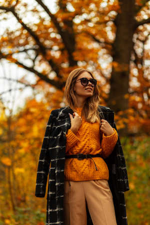 Fashionable caucasian beauty girl with stylish glasses in autumn fashion clothes with coat and sweater outdoorsの写真素材