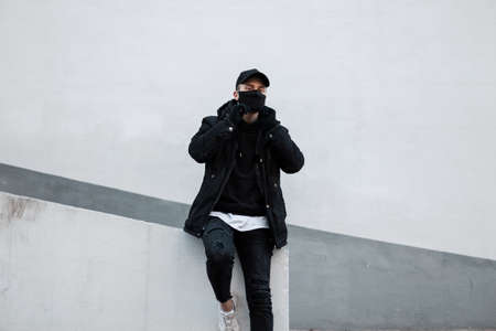 stylish handsome young man model with a protective mask and a black cap in a jacket and a hoodie...