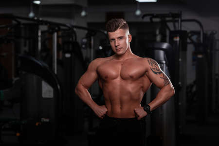 Strong handsome fitness model man with a sports body and tattoo on hand does a workout in the gymの写真素材