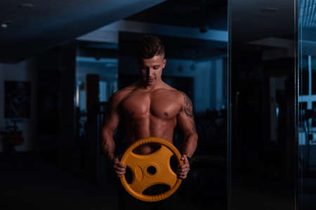 Strong handsome young fitness trainer male bodybuilder with naked torso with muscles doing workout in the darkの写真素材