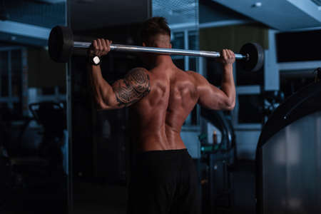 Athletic strong bodybuilder man with bare back and muscles doing exercise in the gym at night