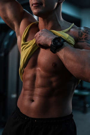 handsome young man athlete with a muscular body shows the belly press against a dark background....