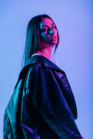 Fashion glamor girl in urban stylish outwear with leather jacket poses in creative studio with blue-pink gradient color lights.の写真素材