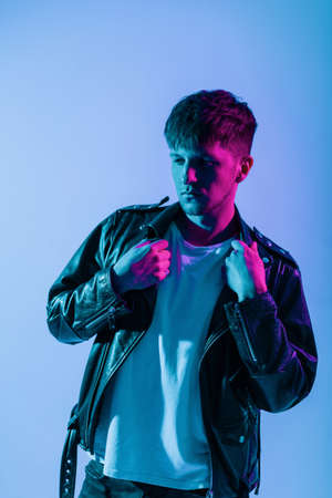 Cool brutal handsome young man with a fashionable hairstyle in a stylish leather retro jacket posing in the studio on neon pink lightの写真素材