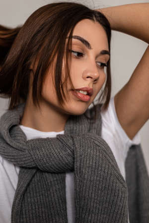 Close-up stylish portrait of a pretty young woman model with a cute face in fashion clothes with a white t-shirt and a vintage knitted sweaterの写真素材