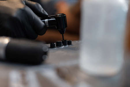 Professional man tattoo artist in black gloves with a mixer mixes paint and ink in tubes, close-up. Preparation for creating a tattooの写真素材