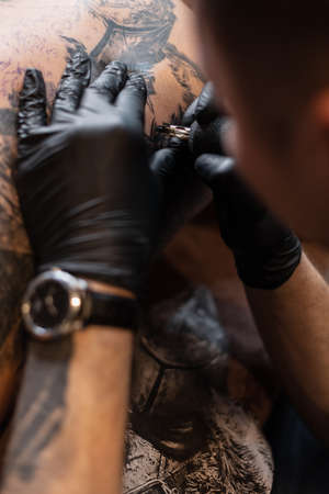 Men's hands of a tattoo artist in black gloves with a tattoo machine gets a tattoo on the skin, close-upの写真素材