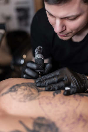 Professional tattoo master man with a tattoo machine stuffs a tattoo on a man's back in the studio. working processの写真素材