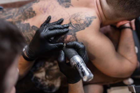 tattoo artist with a modern tattoo machine stuffs a tattoo on the back, close-upの写真素材
