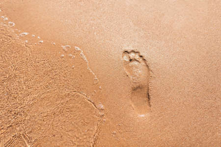 Human footprint in the sand on the beach with a wave near the sea, top view. Summer vacation and rest conceptの写真素材