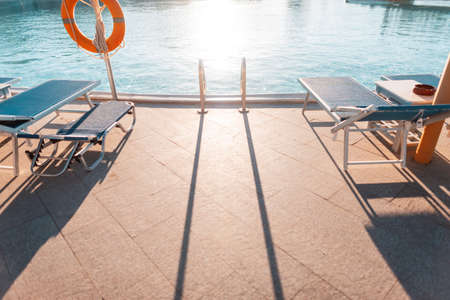 Beautiful pool with a metal handrails descent, beach lounger and a life buoy at sunset. Swimming and summer vacation conceptの写真素材