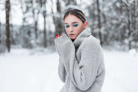 Stylish beautiful young woman model in a vintage gray knitted sweater in the snowy forest on a cold winter dayの写真素材