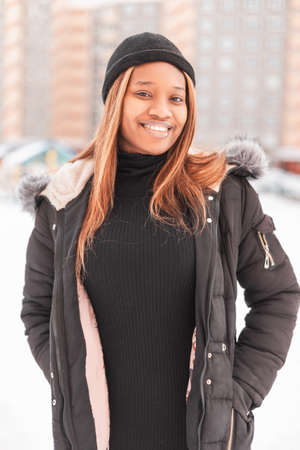 Happy beautiful young black woman with a smile wearing fashionable clothes with a jacket and hat on the streetの写真素材