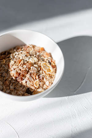 Delicious healthy oatmeal with dried fruits in a white plate on a white plate with early morning sunrise. Raw vegan muesliの写真素材