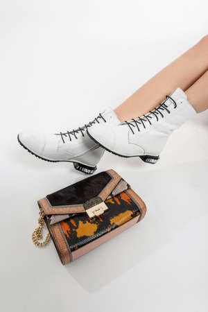 Beautiful female legs with long white leather shoes and a fashionable woman's handbag on a white backgroundの写真素材