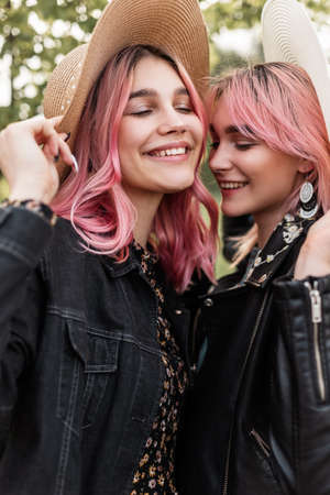 Smiling lovely happy stylish women in trendy youth clothes in fashion straw hats posing outdoors outside city on sunny day. Pretty cheerful girls with positive smiles enjoy holidays in countryside.の写真素材