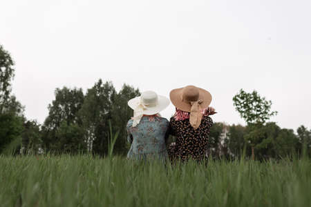 Two beautiful women in straw hats in blue and black dress with floral stylish pattern rests on green...
